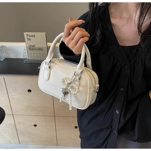 Close-up of cream white Boston bag with pearl bow charm and silver heart pendant detail