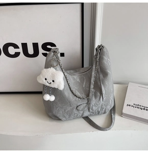 Detail of grey pleated shoulder bag featuring a silver metal chain and plush cloud charm