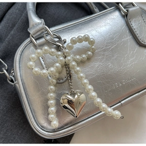 Close-up of silver wrinkled leather handbag with pearl bow and heart charm details
