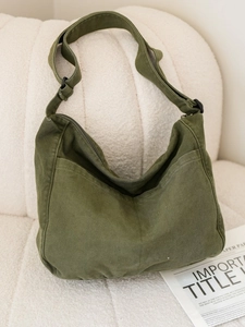 Large army green nylon messenger bag with adjustable strap on a soft white sofa