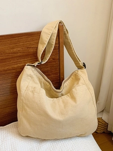 Large beige nylon messenger bag with adjustable strap in a cozy home bedroom setting