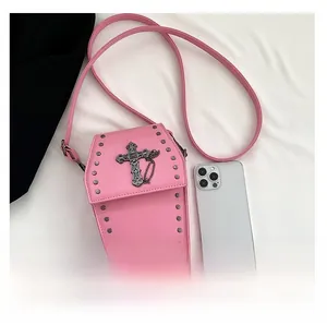 Pink coffin crossbody bag with gothic cross and rivets next to a smartphone