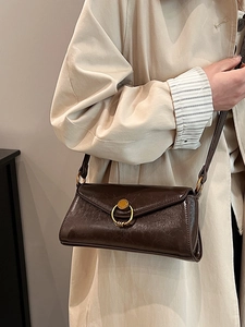 Brown leather baguette bag with gold metal buckle shown on a trench coat shoulder