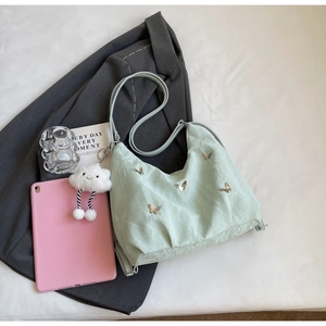 Mint green nylon crossbody bag with metal butterfly detail and white plush cloud charm