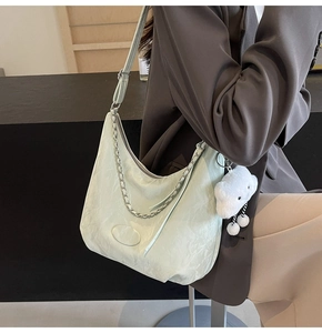 Detail of light green crescent shoulder bag with silver chain and white plush charm on model