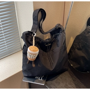 Detail of black nylon tote bag featuring a coffee cup plush charm and adjustable strap