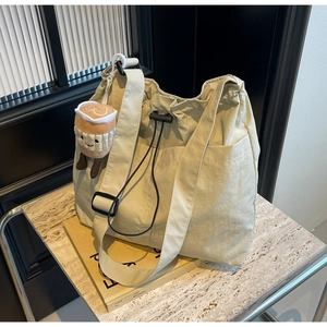 Detail of beige nylon tote bag with side pocket and coffee cup plush charm on books