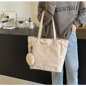 Detail der beigen Nylon-Tragetasche mit Vordertaschen und rundem Münzfach-Anhänger