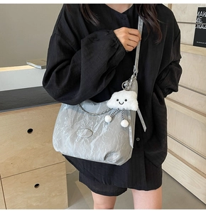 Detail of silver pleated shoulder bag featuring metal chain and a white cloud plush charm