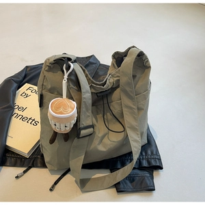 Olive green nylon tote bag featuring drawstring detail, adjustable strap and plush charm