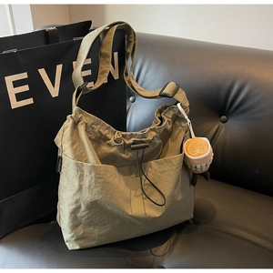 Olive green nylon tote bag featuring a cute plush pendant and drawstring detail on a sofa