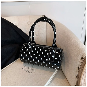 Close-up detail of glossy black patent leather cylinder bag with stylish white polka dots