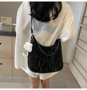 Detail of black pleated shoulder bag with silver chain and white plush charm on model