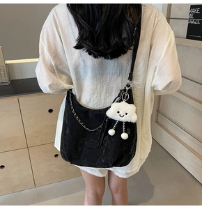 Detail of black half-moon crossbody bag with silver chain and white plush charm on model