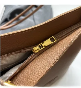 Detail of golden metal zipper and brown litchi pattern leather on a crossbody bag