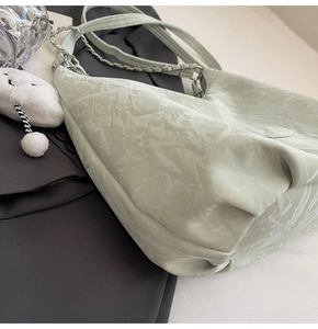 Detail of light green bag showing unique pleated texture and chain strap with cloud charm