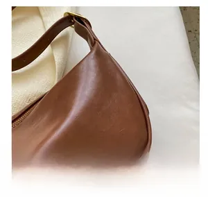 Dettaglio borsa a mezzaluna in pelle marrone con cerniera dorata e logo stampato BAGS
