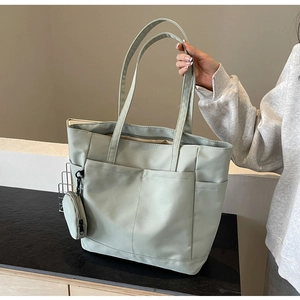 Detail der salbeigrünen Nylon-Tragetasche mit Vordertaschen und passendem Münzetui-Anhänger