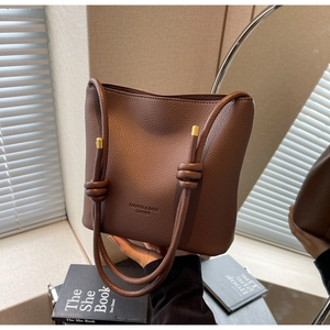 Detailed view of dark brown pebbled leather bucket bag with knotted strap and gold hardware