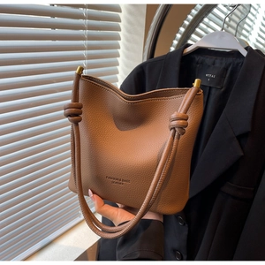Detailed close-up of brown litchi grain leather bucket bag with knotted shoulder strap