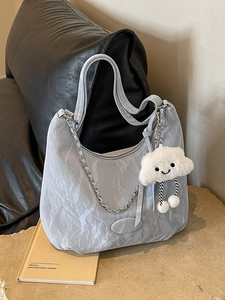 Light blue pleated tote bag with silver chain strap and cloud charm on a stone table