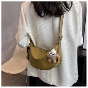 Borsa a tracolla a mezzaluna verde oliva con ciondolo mostro su un blazer bianco