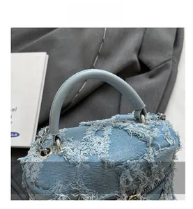 Detail of light blue denim bucket bag with frayed fringe texture and silver metal chain strap