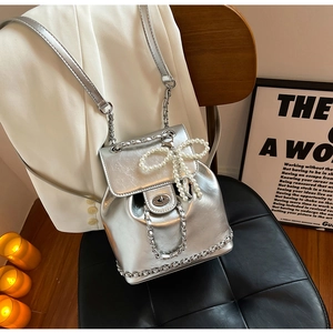 Detail of silver metallic backpack featuring a pearl bow charm and chain decoration