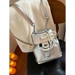 Silver metallic chain backpack with pearl bow charm on a leather chair background