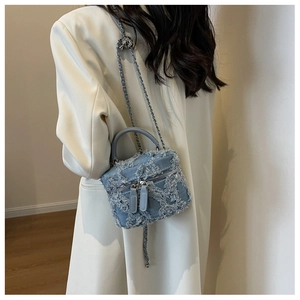 Close-up of denim mini bucket bag featuring frayed fringe edges and metal chain strap