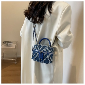 Detailed view of denim vanity bag with fringed diamond pattern and chain strap on a model