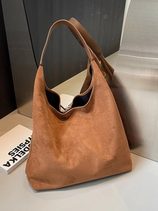 Borsa hobo minimalista in camoscio marrone con ampia tracolla in pelle su un tavolo moderno