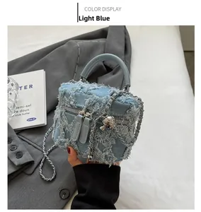 Detail of light blue denim square bag with vintage frayed edges and silver double zippers