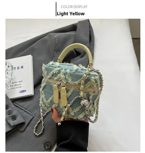 Detail of blue denim crossbody bag with yellow trim, fringe texture and silver chain strap