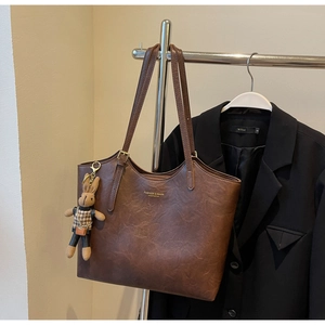 Detail of a brown leather tote bag featuring a cute bunny charm and golden text logo