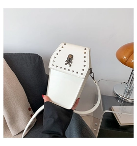 Handheld view of a white coffin-shaped gothic crossbody bag with skull and stud details