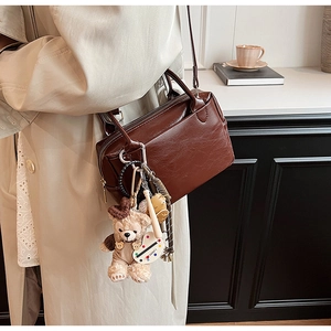 Détail d'un sac Boston en cuir marron foncé brillant avec charm ours en peluche et anses