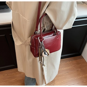 Détail du sac à main bordeaux en cuir avec breloque baseball sur un manteau beige