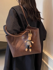 Vintage brown leather tote bag with rabbit charm worn by a model in a black coat