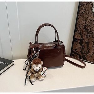 Détail du sac Boston en cuir poli marron foncé avec un charmant ours en peluche attaché