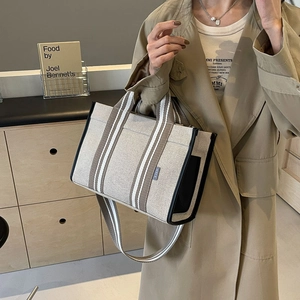 Detail view of large canvas tote bag with beige brown stripes and leather edging
