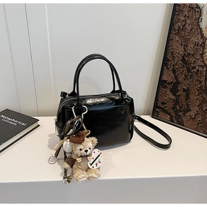 Détail du sac à main noir brillant avec charm ours en peluche et bandoulière