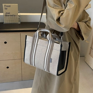 Detail of canvas tote bag with striped handles and side brand tag on a neutral background