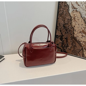 Gros plan d'un sac à main en cuir verni bordeaux avec poignées et fermeture éclair en métal