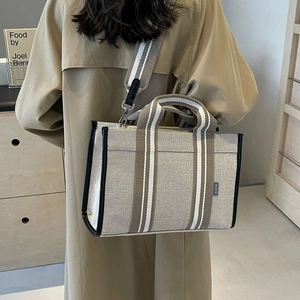 Detail of beige canvas tote bag with striped straps shown on shoulder in a lifestyle setting