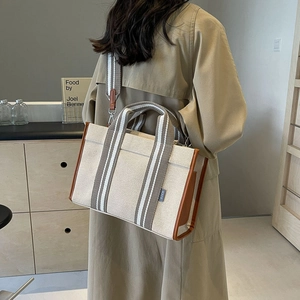 Detail of canvas tote bag showing striped handles and leather trim on beige fabric