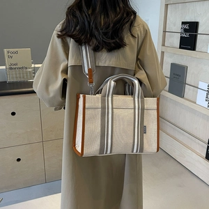 Detail of canvas tote bag with brown leather trim and striped crossbody shoulder strap