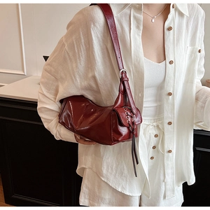 Detail of dark red faux leather shoulder bag with metallic eyelets and silver drawstring