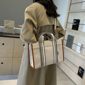 Detailed side view of canvas tote with brown leather trim and striped shoulder strap