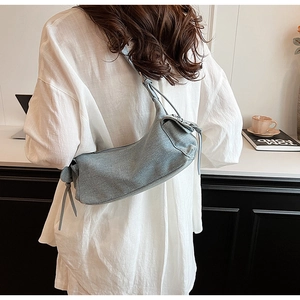 Detail of light blue denim fabric shoulder bag with side drawstring in a casual office setting